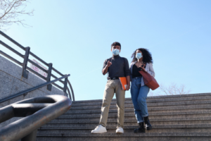 Two college students, masked, are walking down a unversity's steps