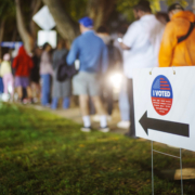 Elections in Los Angeles, California. “I Voted” sign with voters standing in line on sidewalk in the background as many people are voting late at night.